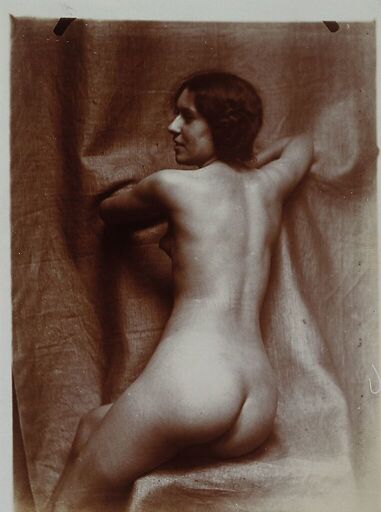 Naked woman sitting three-quarters back, on a chair, face in profile left